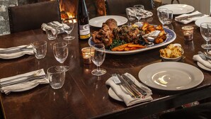 A dining table set with plates, glasses, and cutlery, a fireplace with antlers mounted on the wall, and a framed picture above the fireplace. - The Lamb Inn (Chipping Norton)