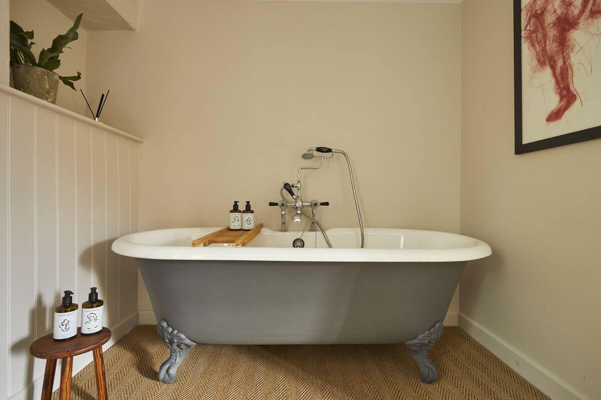 A bathroom with a freestanding bathtub, a wooden stool with toiletries, and a plant on a shelf.