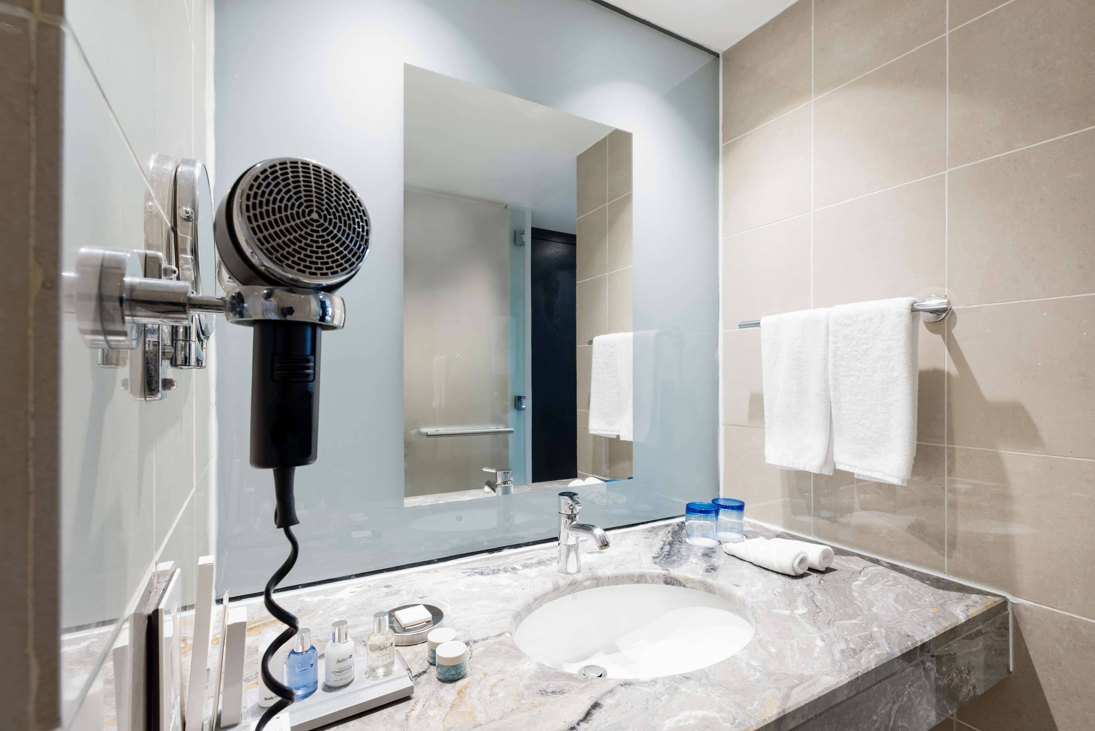 A modern bathroom with a large mirror, a hairdryer, a sink, and two towels hanging on the wall.
