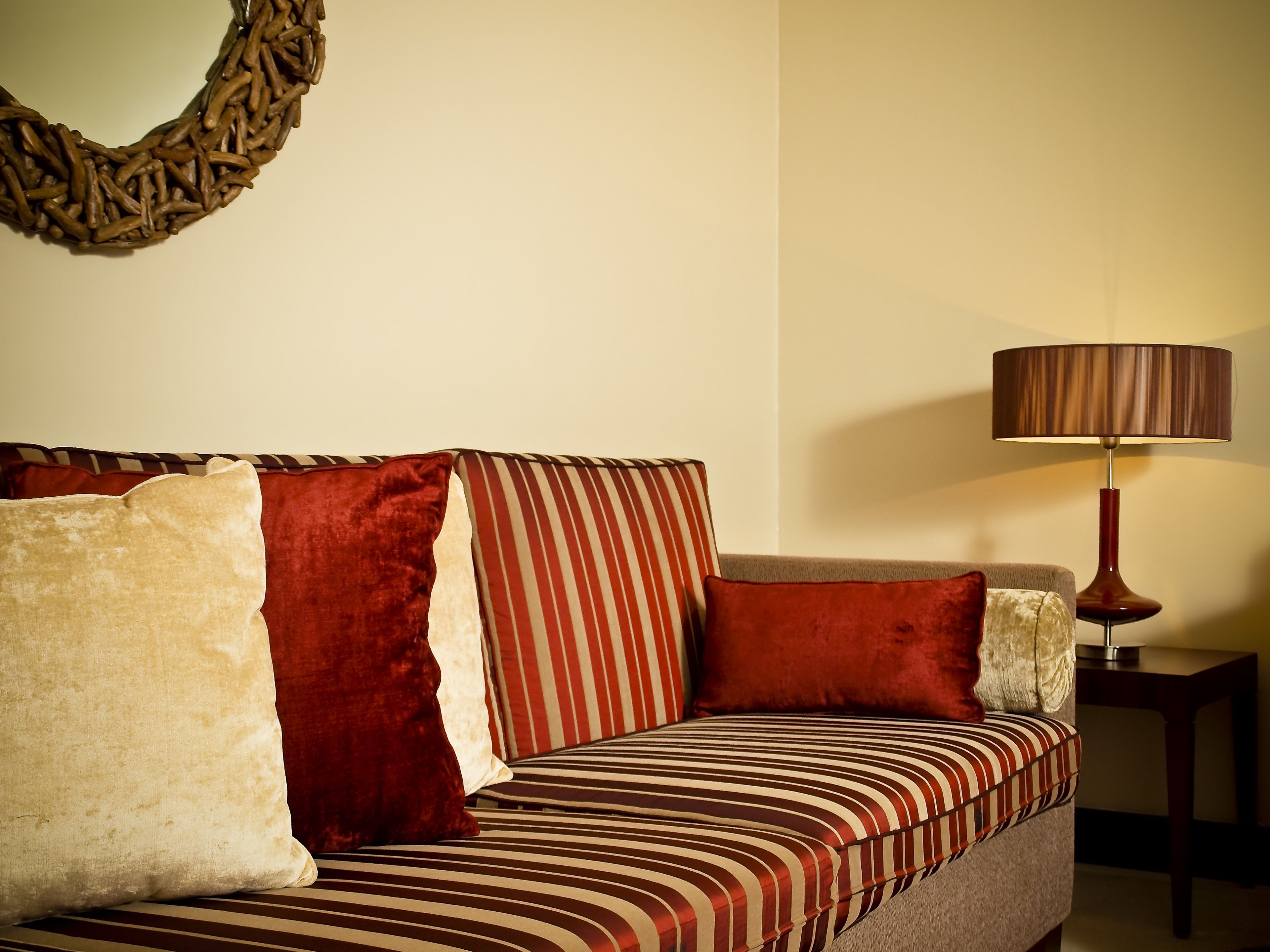 A sofa with striped upholstery, a round woven wall decoration, and a table lamp.