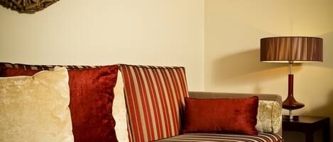 A sofa with striped upholstery, a round woven wall decoration, and a table lamp.