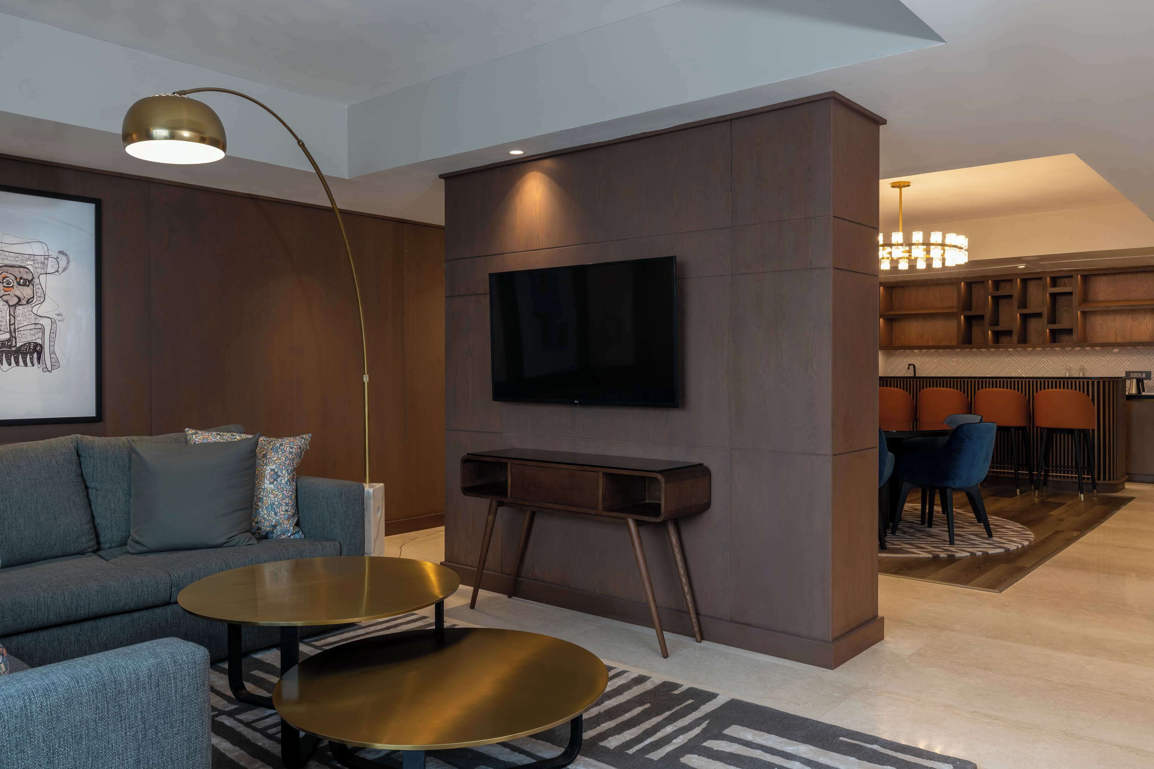 Uma sala de estar moderna com sofá, mesa de centro, televisão e um espaço de jantar com cadeiras e lustre.