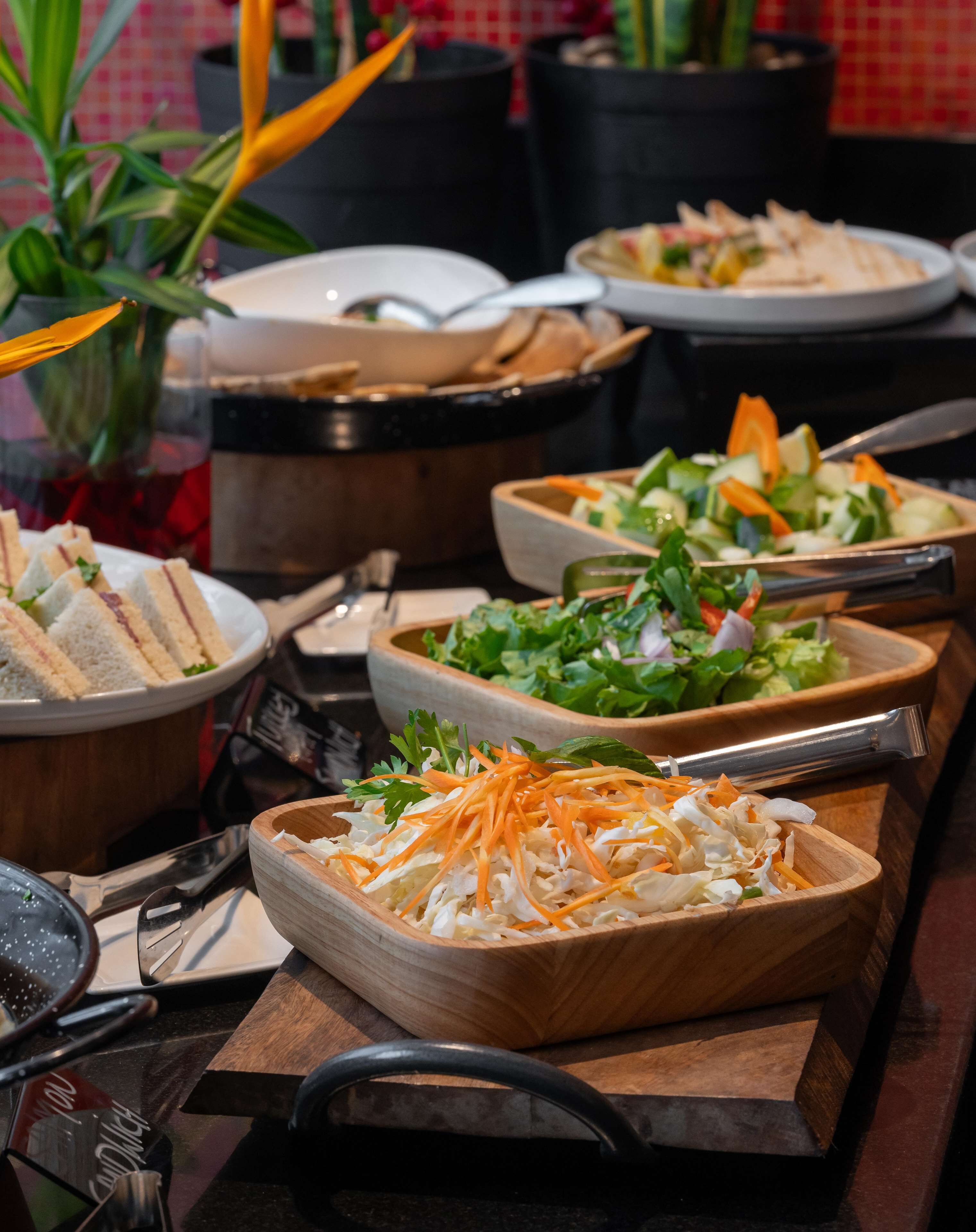 A buffet table with various dishes including sandwiches, salads, and a bowl of shredded vegetables.