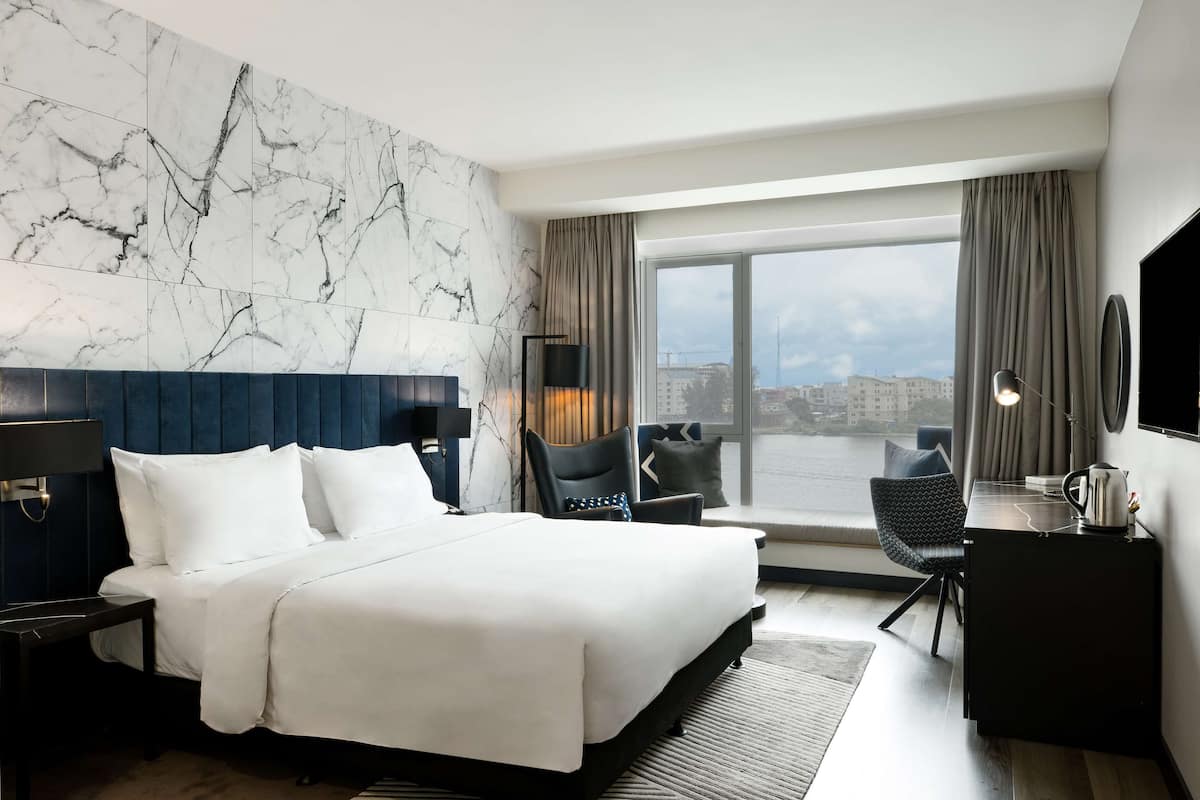 A modern hotel room with a large bed, a desk, and a view of the city.