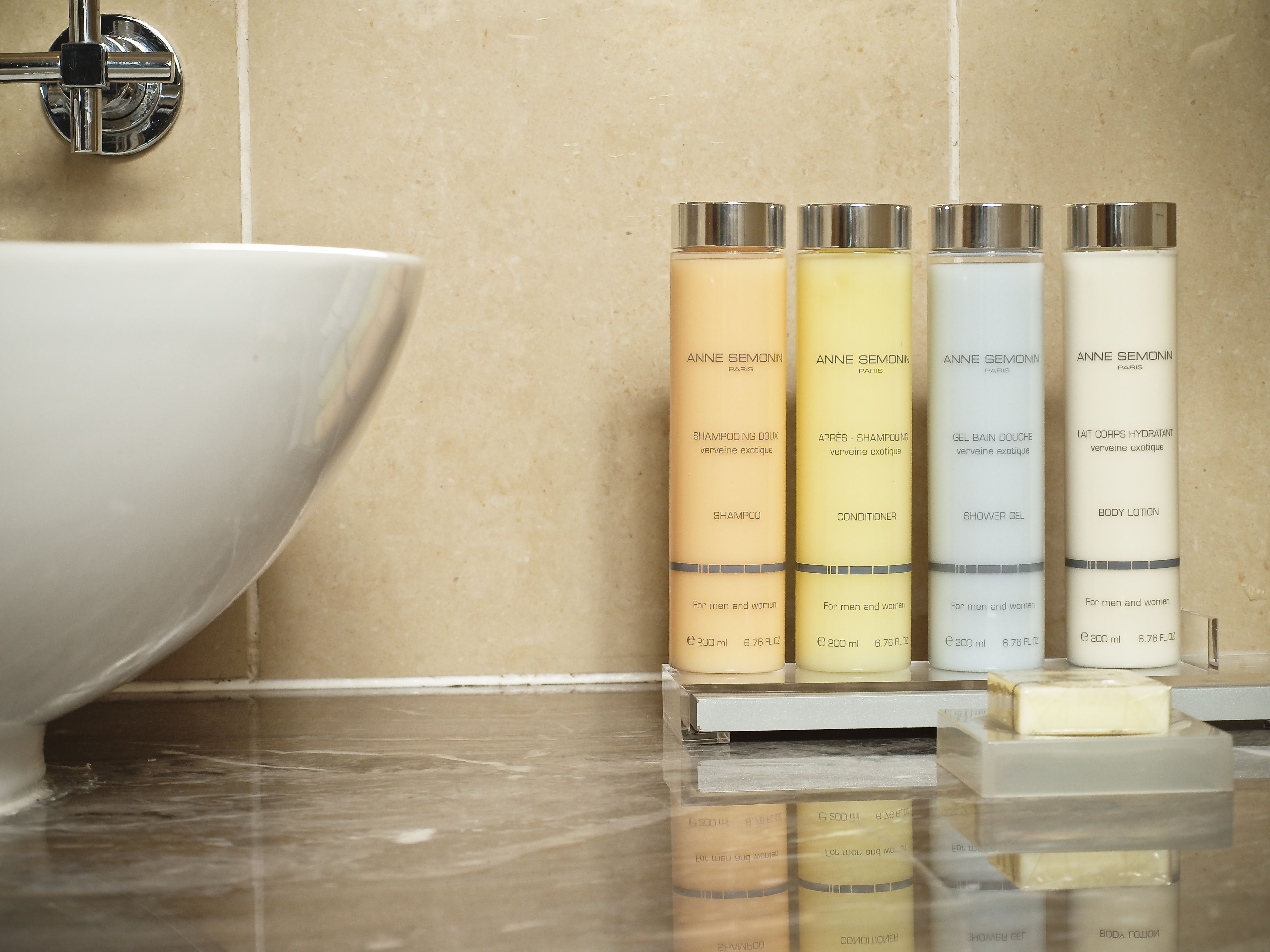 A bathroom with a large white sink and four bottles of Anne Semonin products on a shelf.