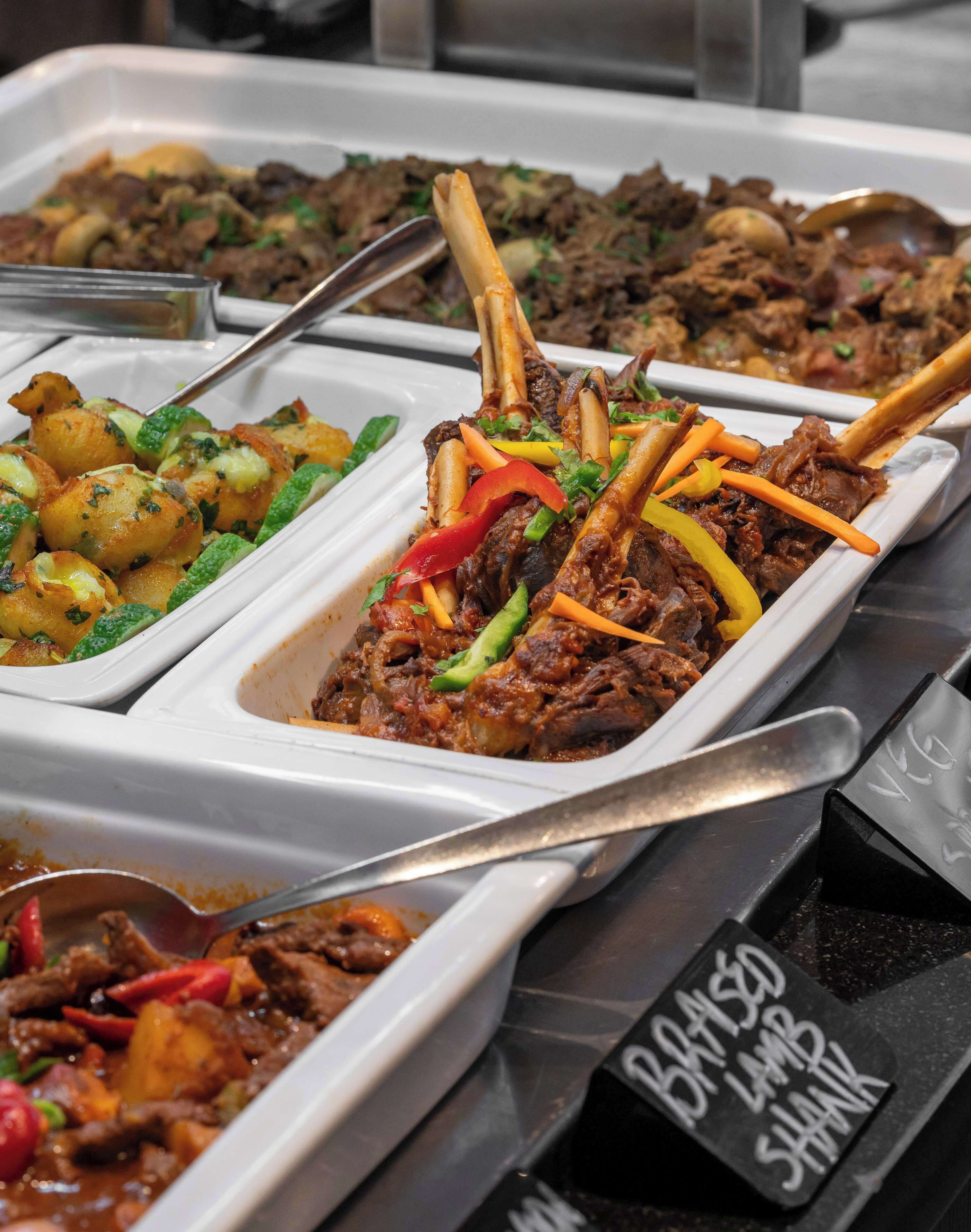 A buffet with various dishes including roasted potatoes, meat with vegetables, and a sign indicating vegetarian options.