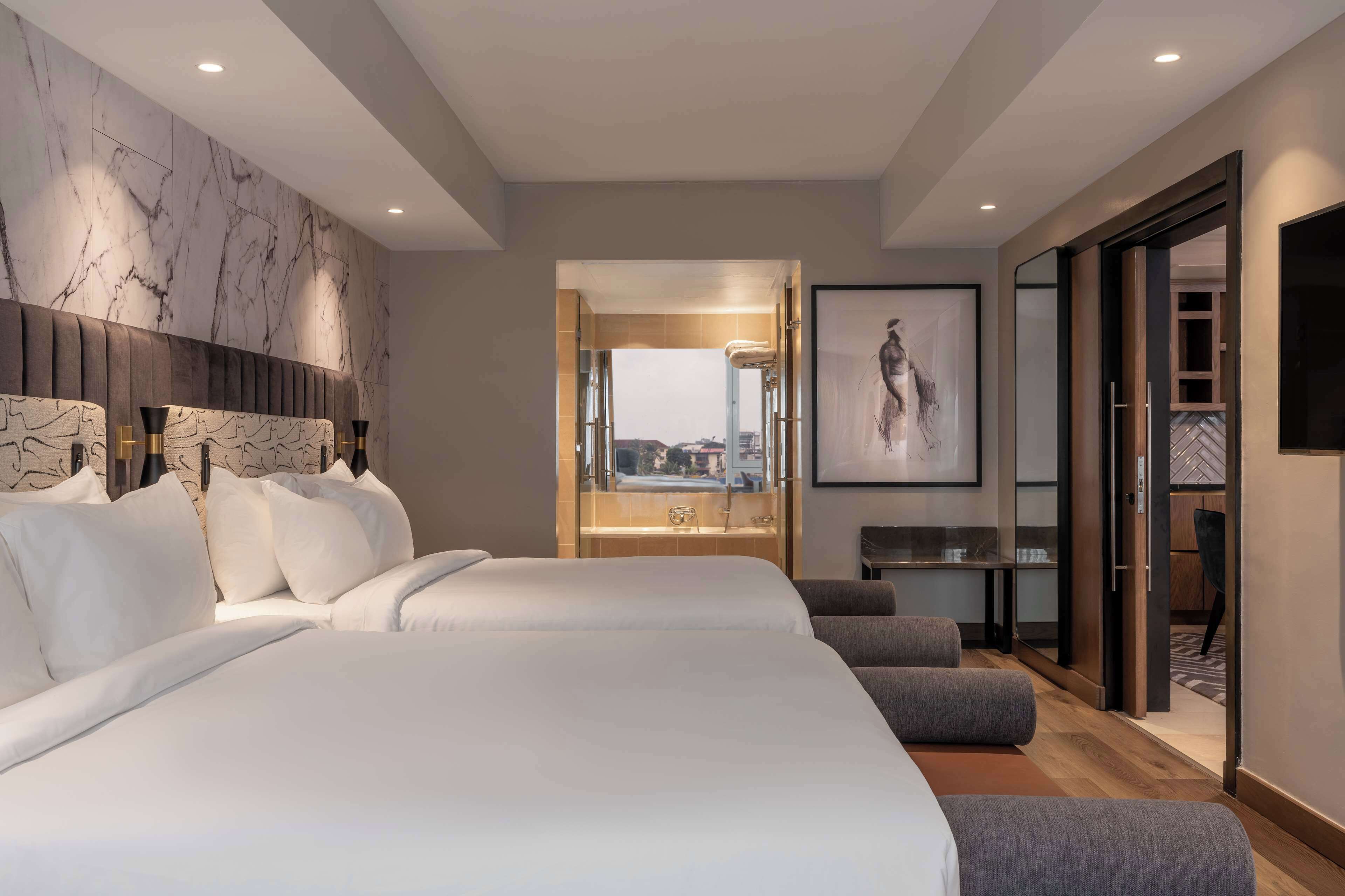 A modern hotel room with a large bed, a sitting area, and a view of the city.