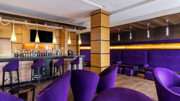 Een bar met paarse zitplaatsen, een bar inrichting met diverse flessen en hangende lampen.