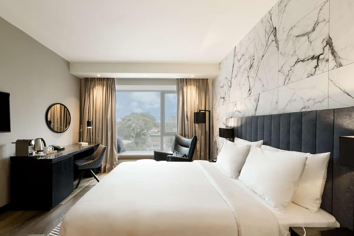 A hotel room with a large bed, a desk, a chair, and a view of the outdoors.