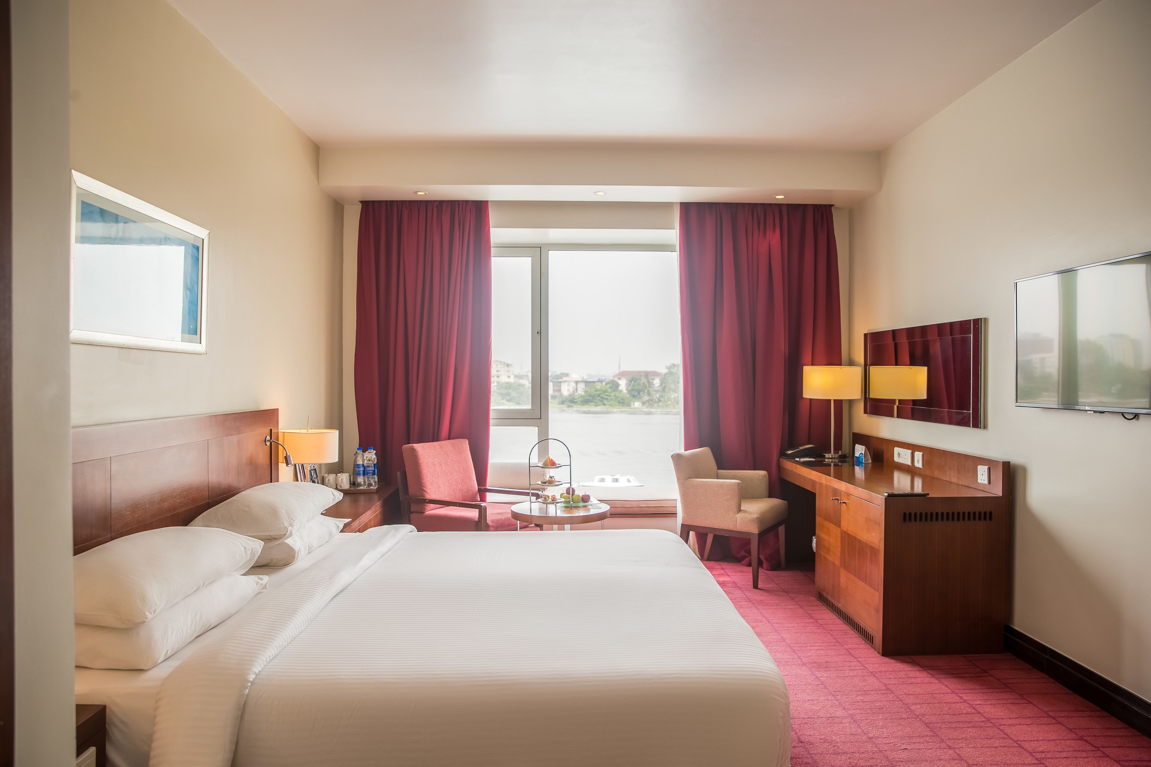 A hotel room with a large bed, two chairs, a desk, and a window with curtains.