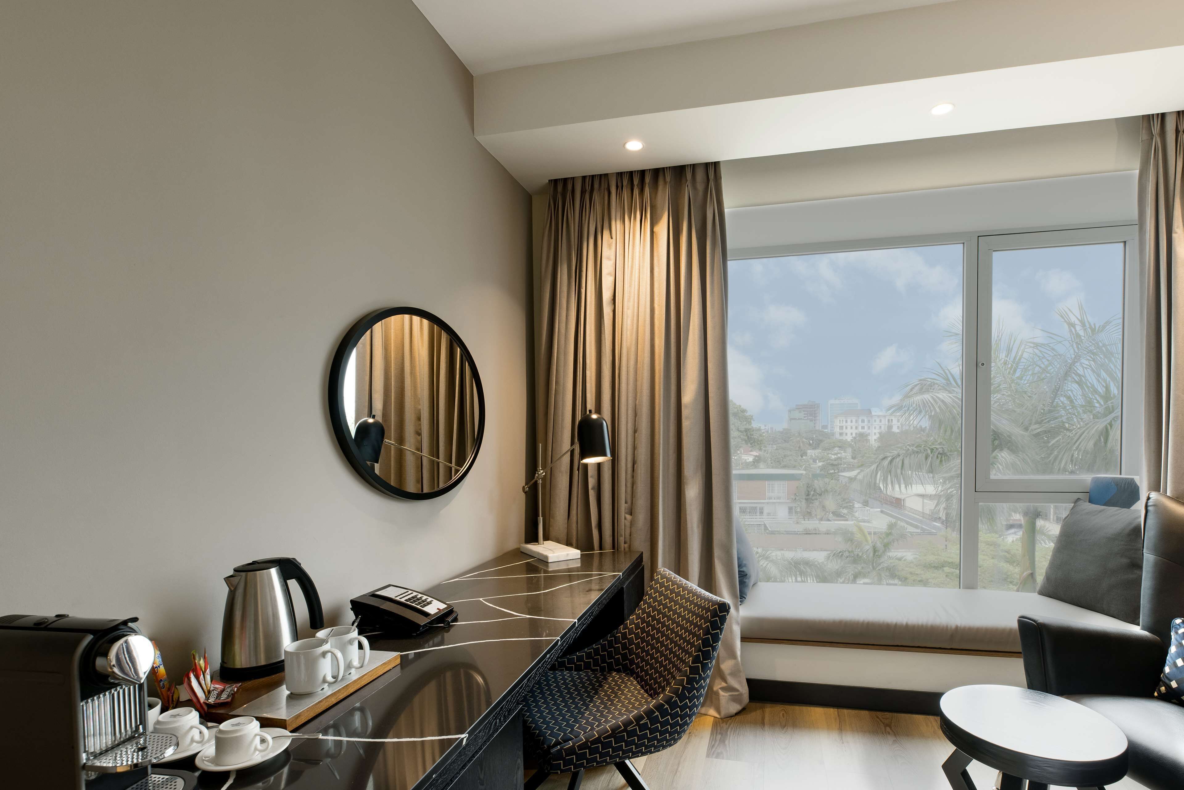 A modern hotel room with a desk, coffee maker, and a view of palm trees through large windows.
