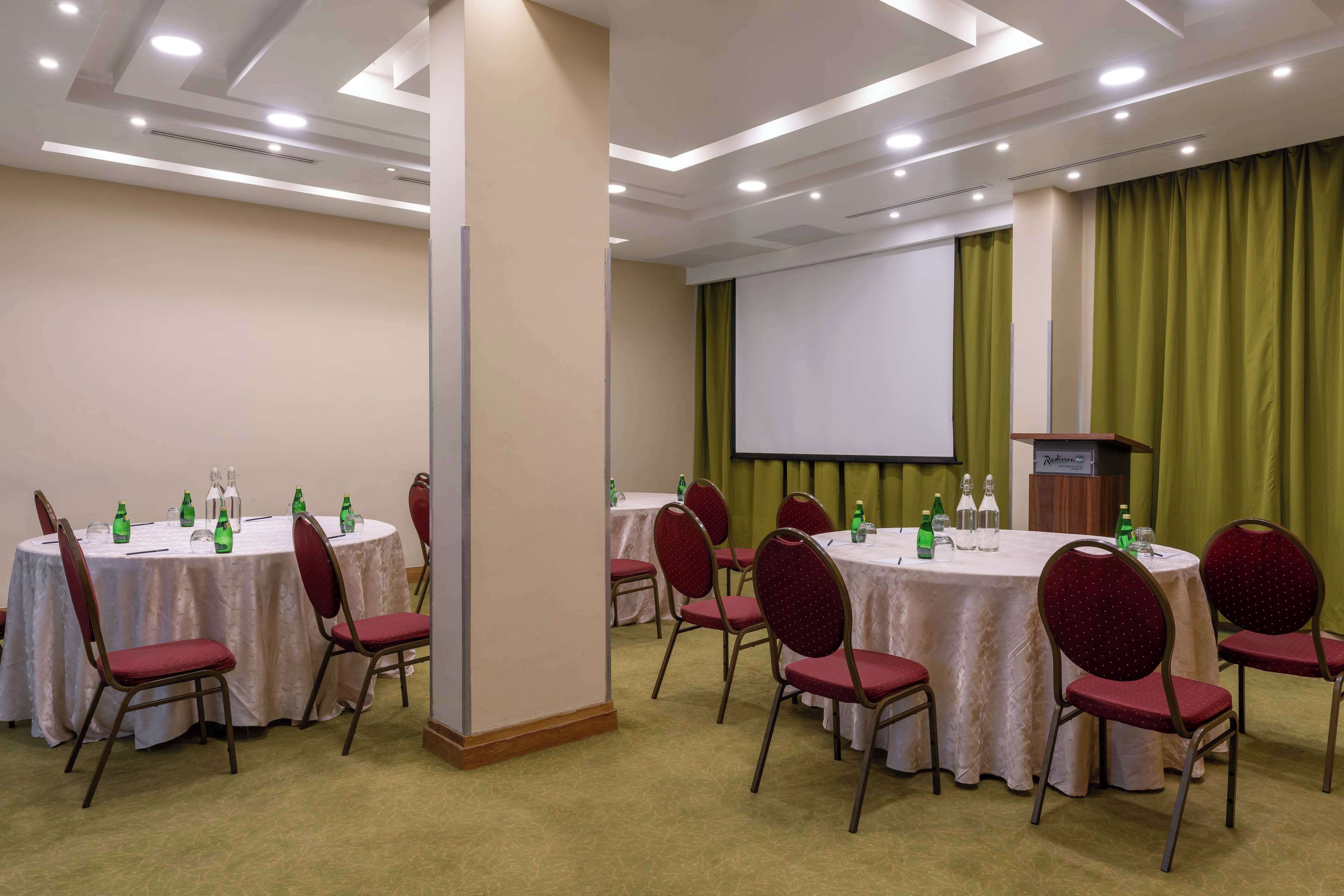 Un salón de conferencias con mesas redondas, sillas rojas y una pantalla de proyector.