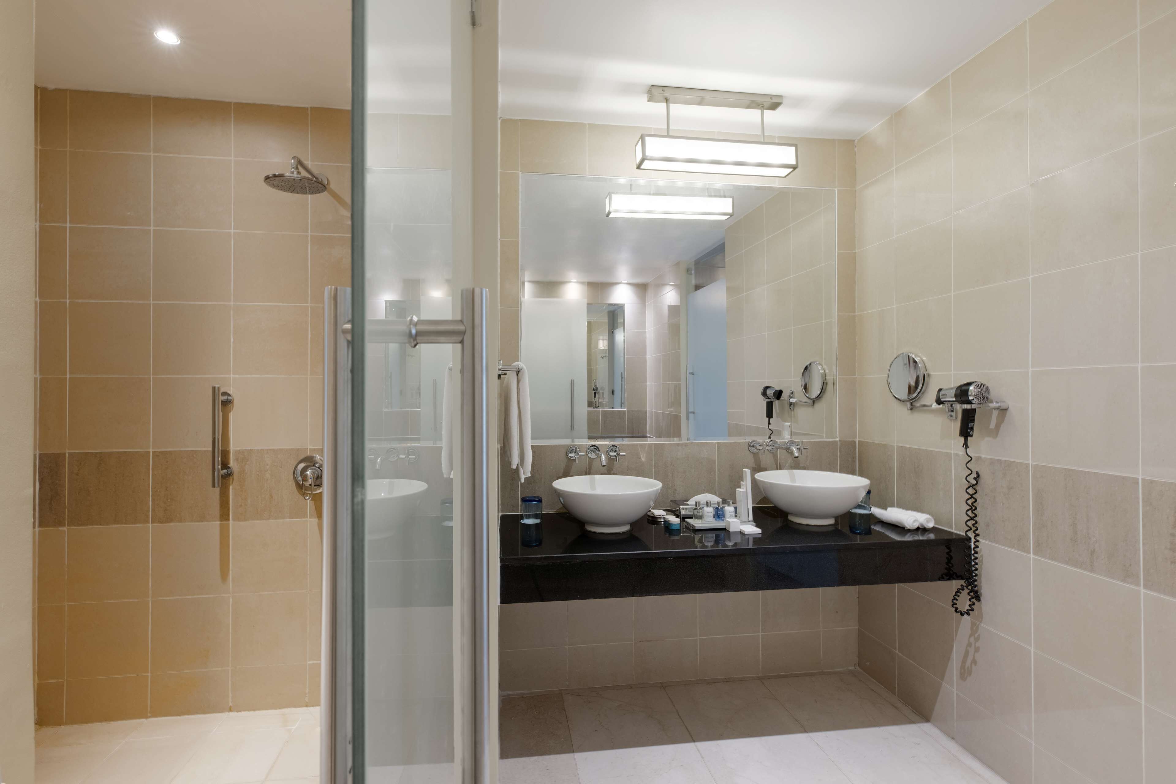 Une salle de bain moderne avec deux vasques, une douche à l’italienne en verre et un grand miroir.