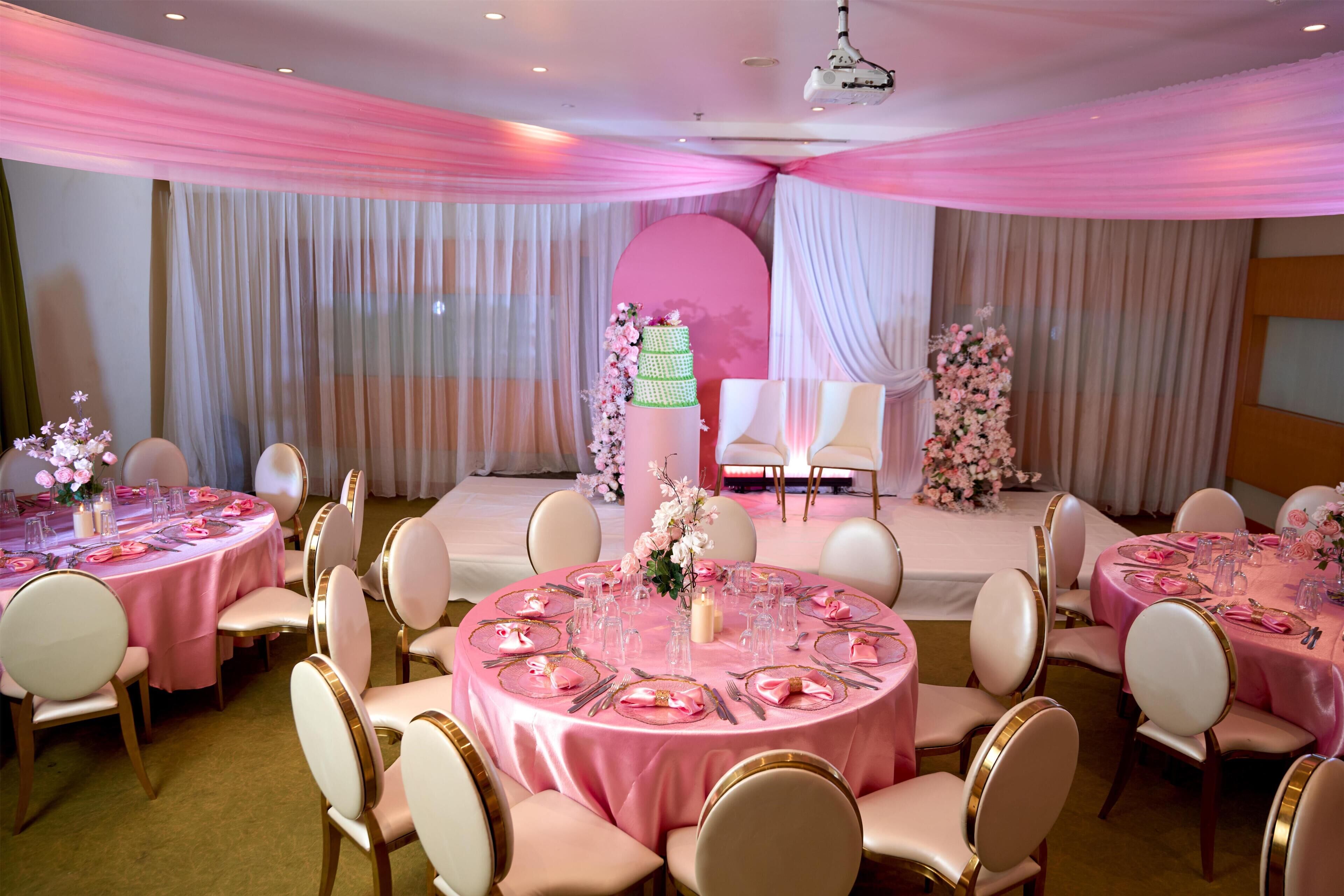 Une salle de banquet avec des tables rondes, des chaises blanches et des nappes roses.