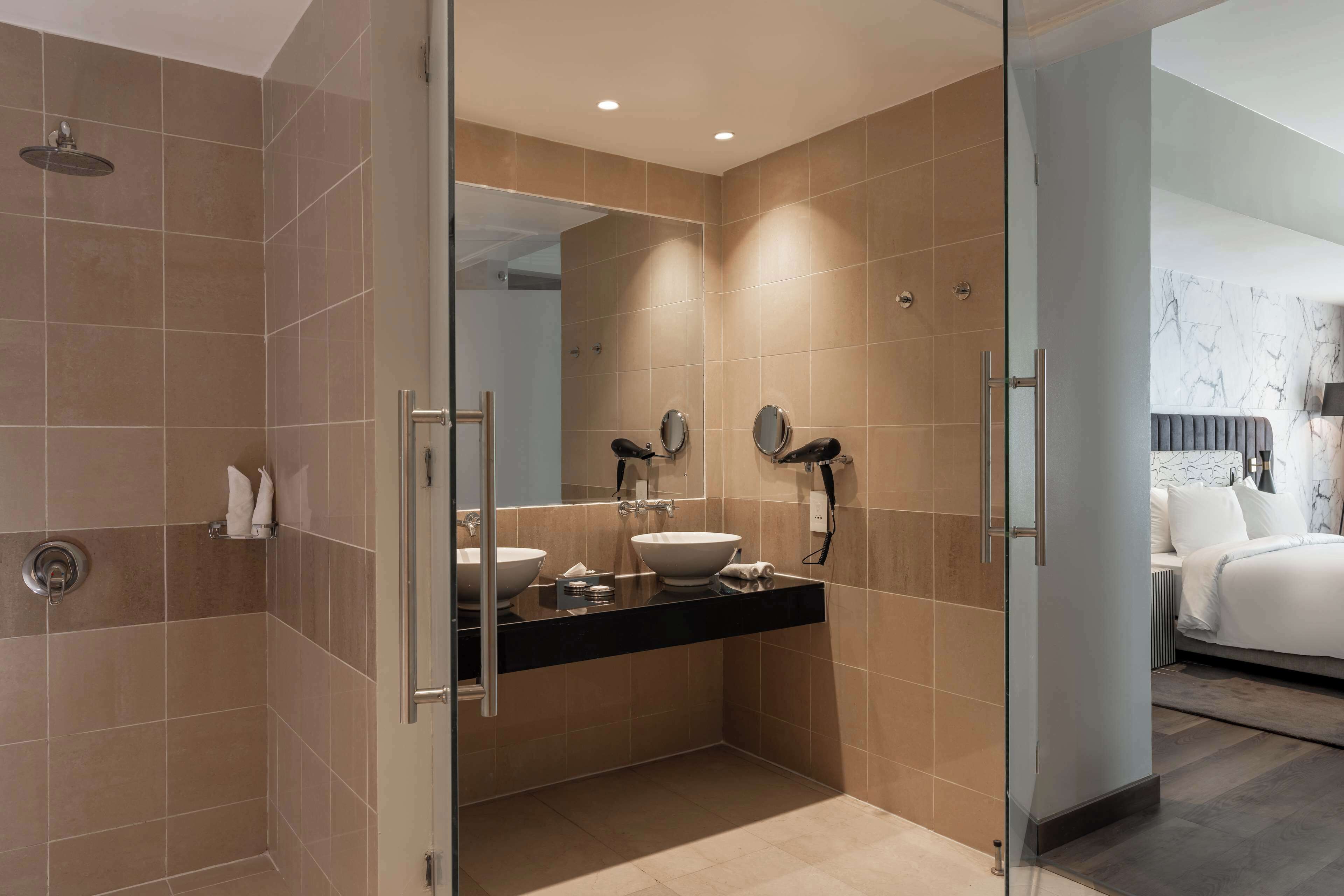 A modern bathroom with a glass shower enclosure, a black countertop with two sinks, and a large mirror.