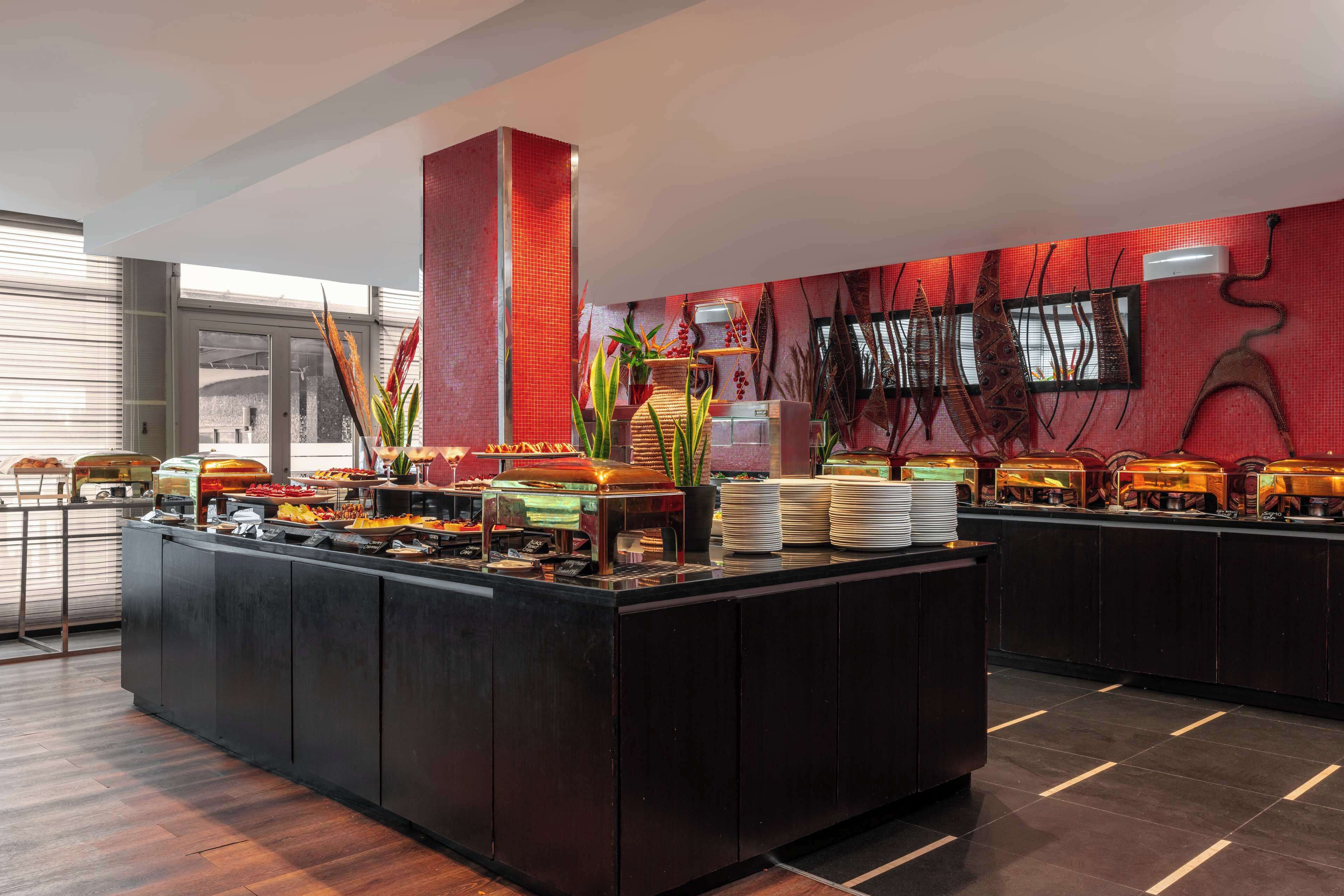 A buffet area with a variety of food options, a tall red pillar, and a wall with abstract art.