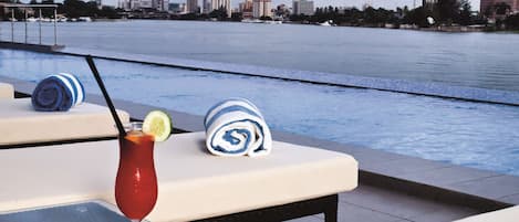 A poolside area with lounge chairs, a table with a drink, and a city skyline in the background.