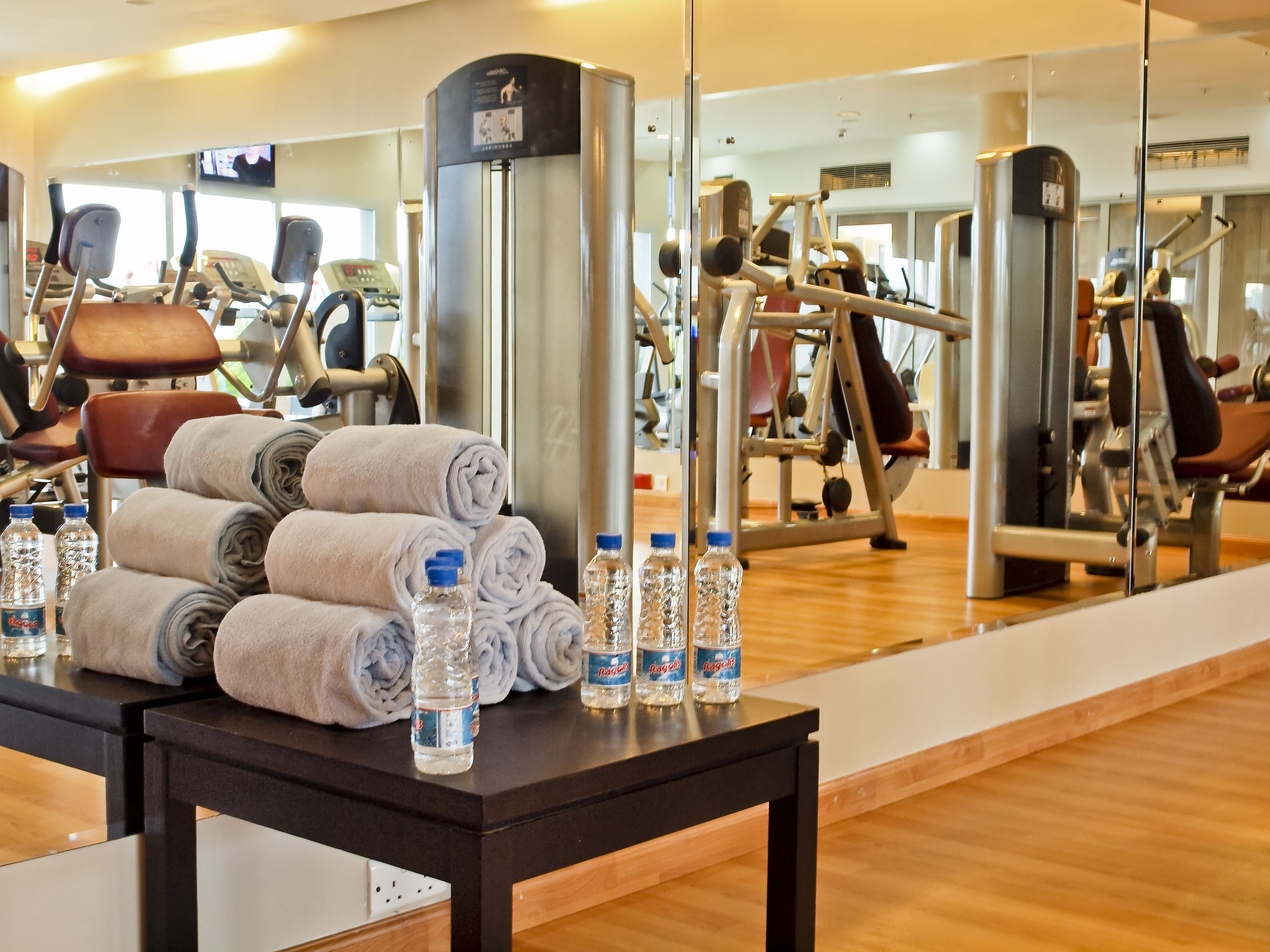 A gym with exercise equipment, a mirror, towels, and water bottles on a table.