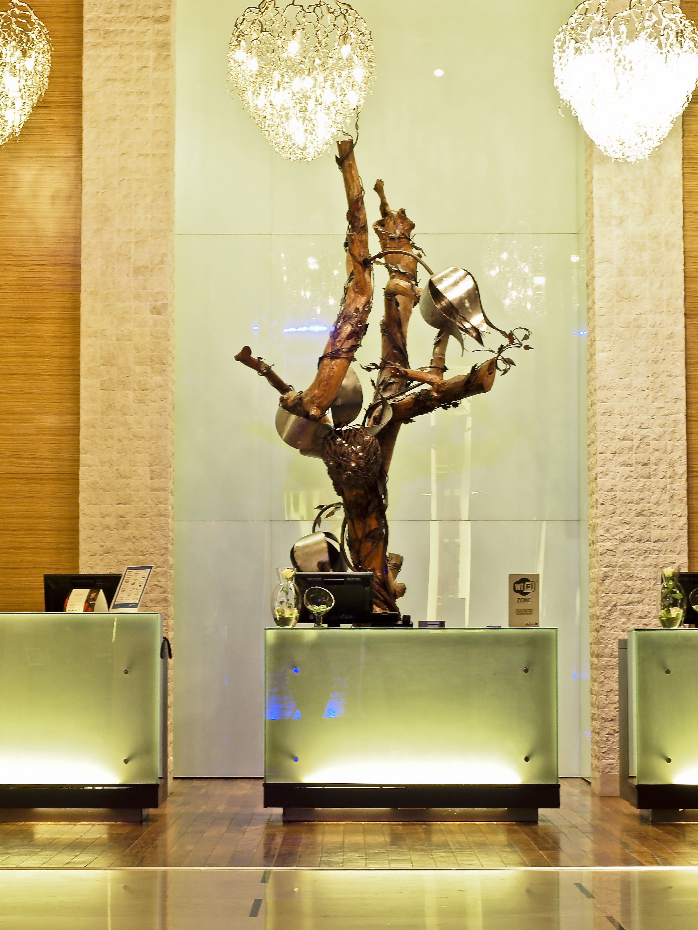 Un mostrador de recepción con una escultura original en forma de árbol, lámparas de diseño moderno y una pared con textura de piedra al fondo.