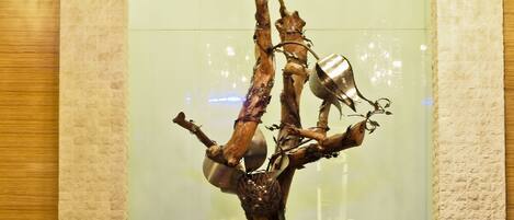 Un mostrador de recepción con una escultura original en forma de árbol, lámparas de diseño moderno y una pared con textura de piedra al fondo.