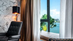 Une chambre moderne avec un fauteuil en cuir noir, un lampadaire et une vue sur l’océan grâce à de grandes fenêtres.