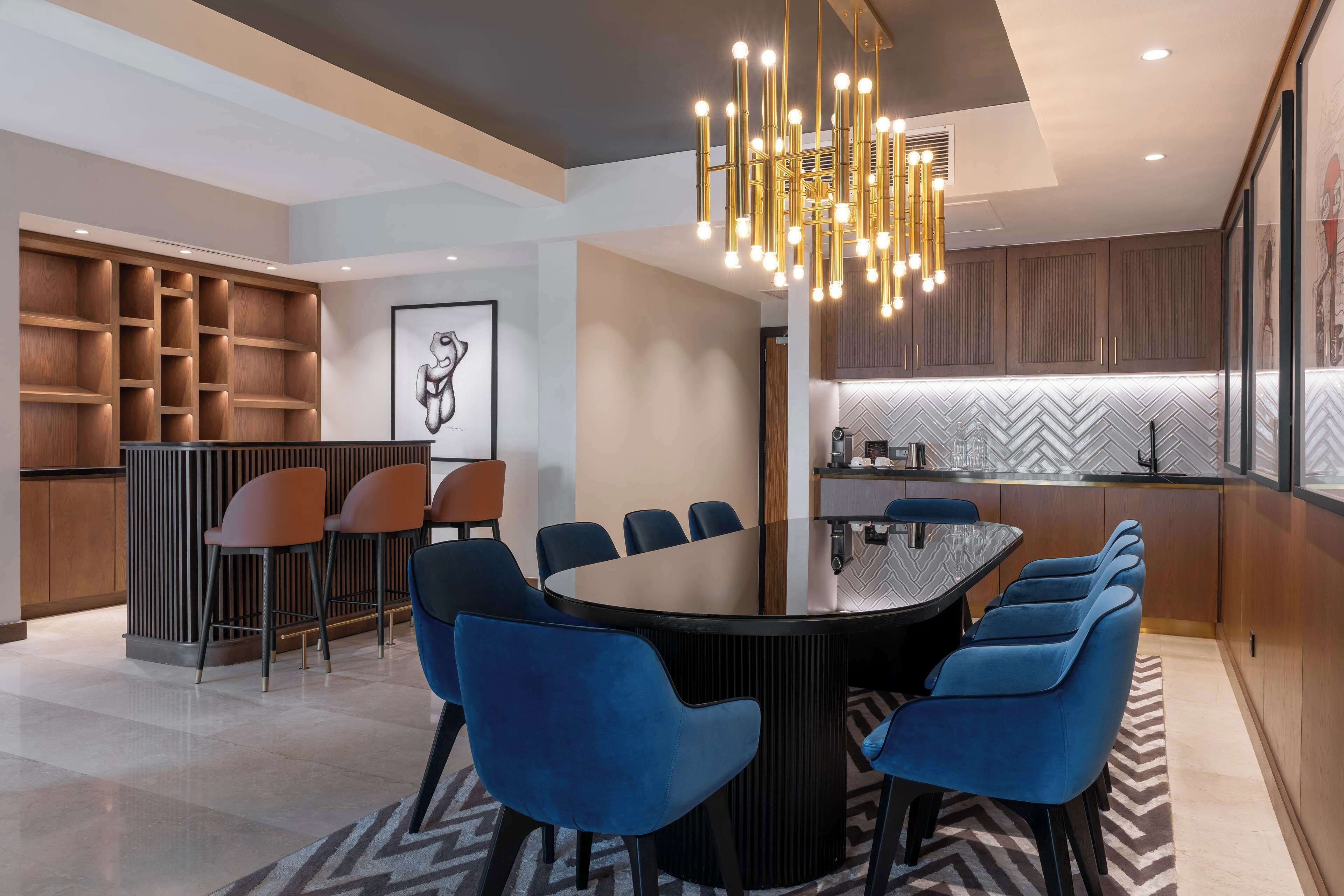 A modern dining area with a round table, blue chairs, and a chandelier.
