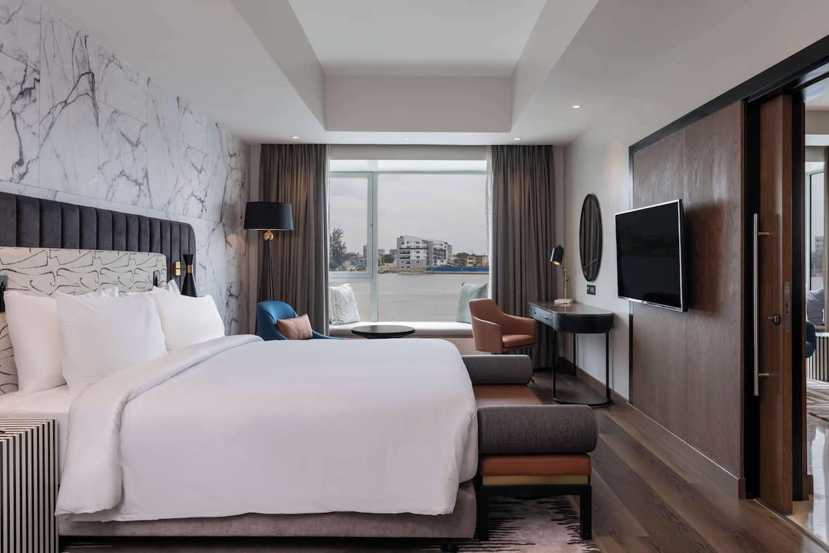 A modern hotel room with a large bed, a desk, a TV, and a view of the city.