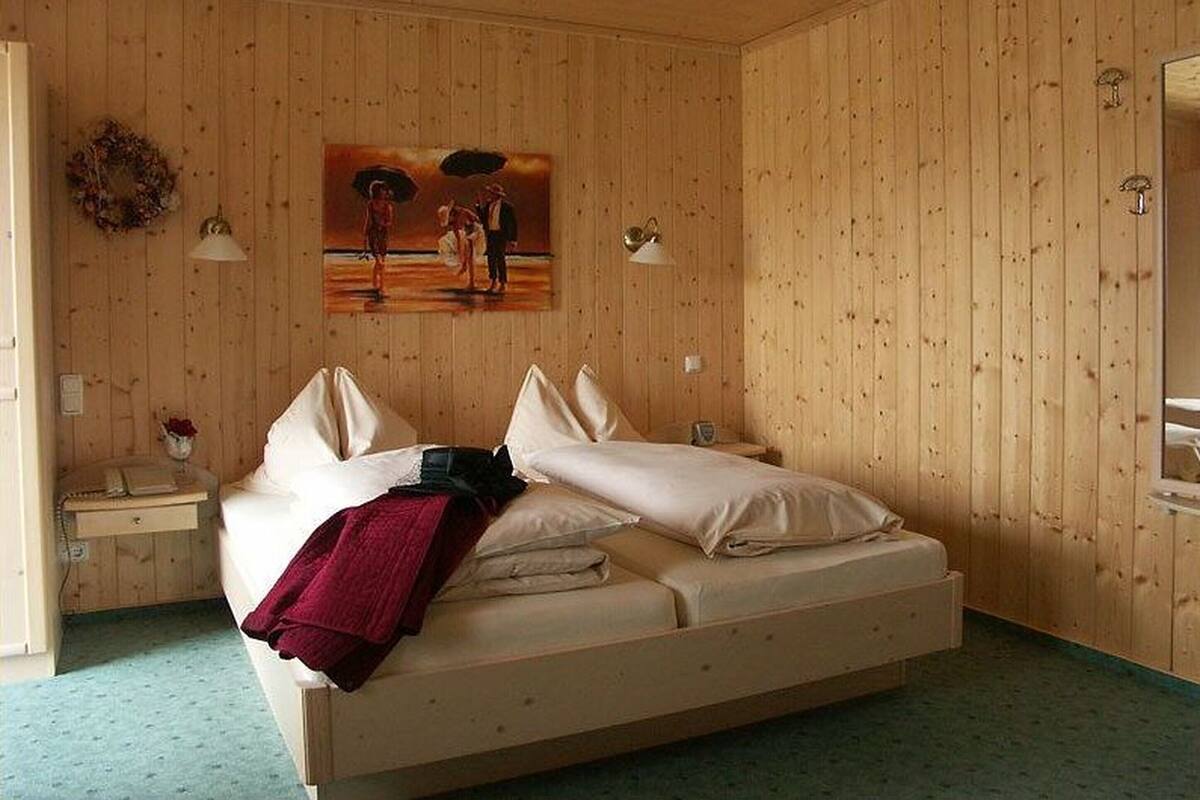 A wooden-paneled bedroom with a bed, two bedside tables, a wall-mounted lamp, and a painting.