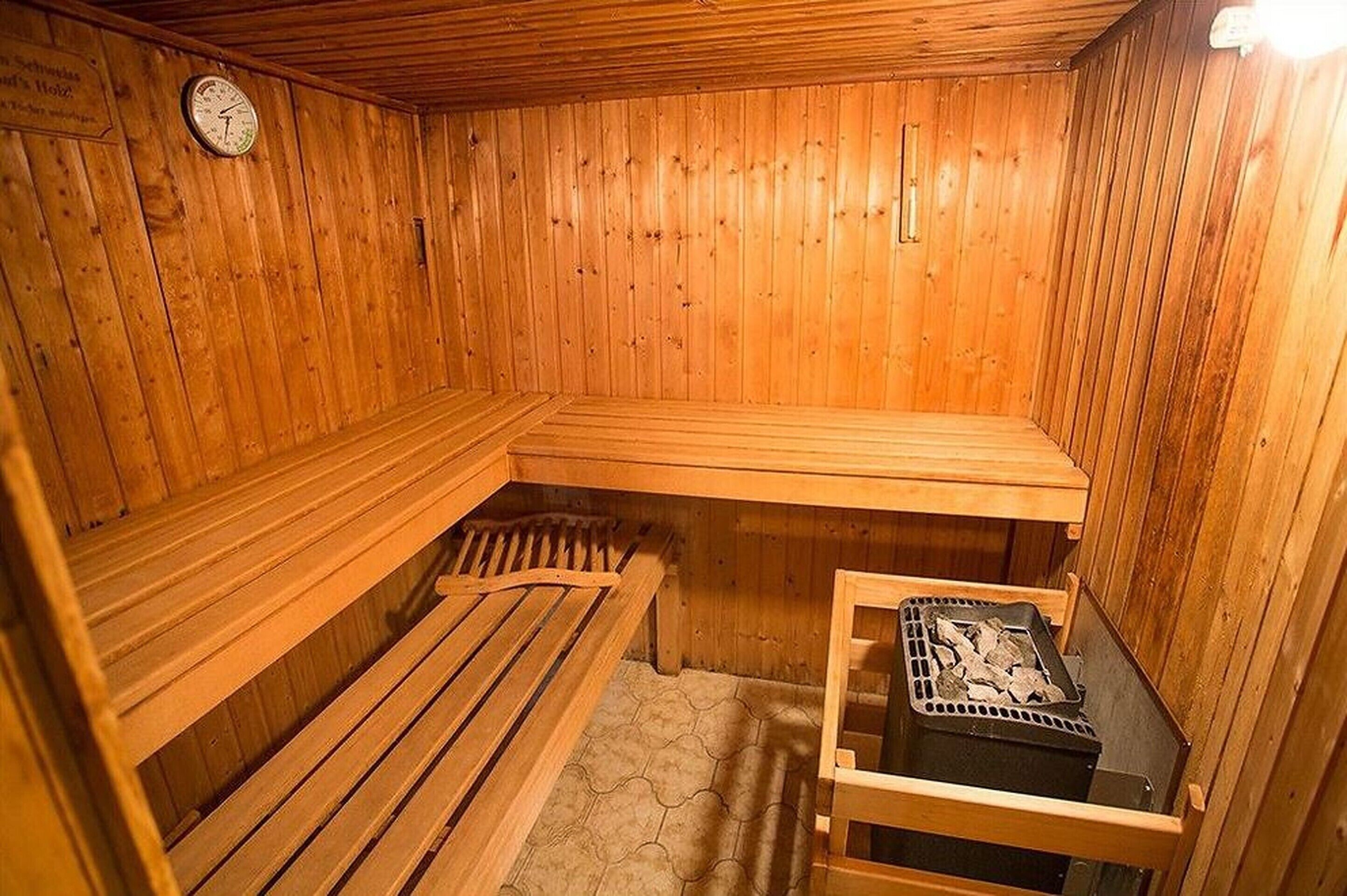 A wooden sauna with benches and a bench seat, a wooden wall clock, and a sauna heater.