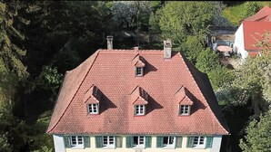 Un bâtiment à deux étages, doté d’un toit recouvert de tuiles rouges, de nombreuses fenêtres avec volets et d’une entrée centrale avec une porte.