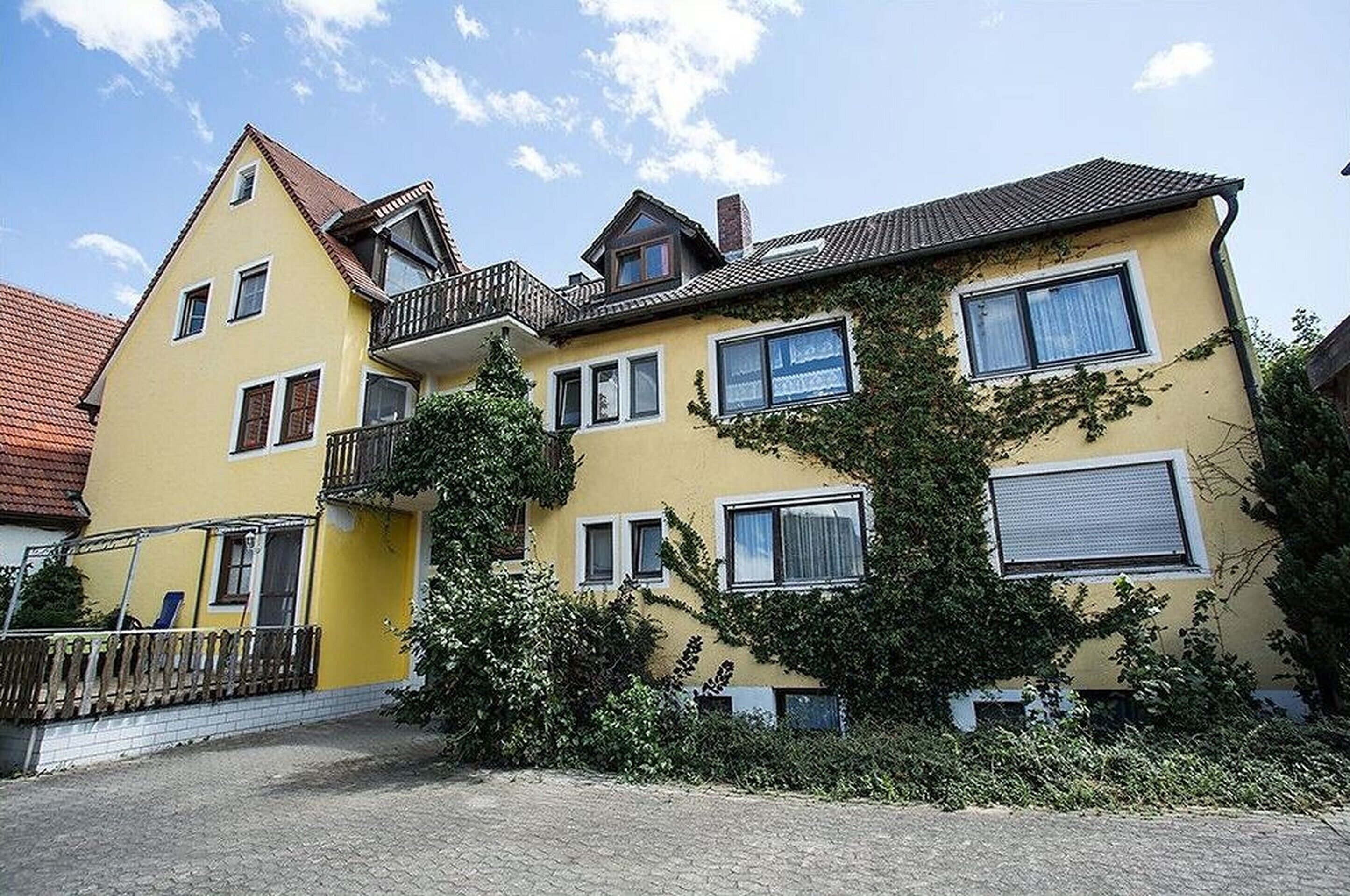 Un edificio amarillo de varios pisos con balcón, ventanas y un pequeño jardín.