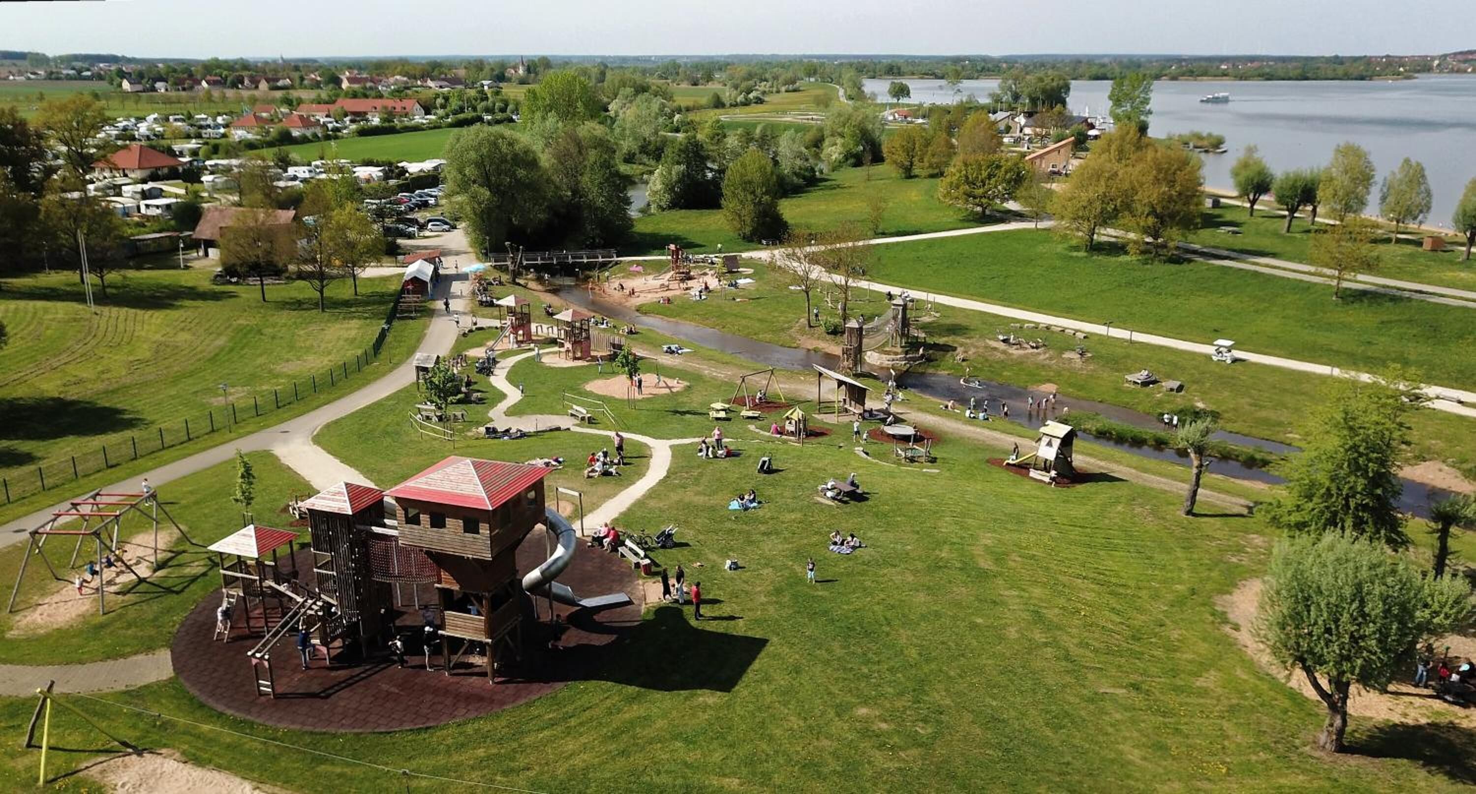 An aerial view of a park with playgrounds, walking paths, and a river.