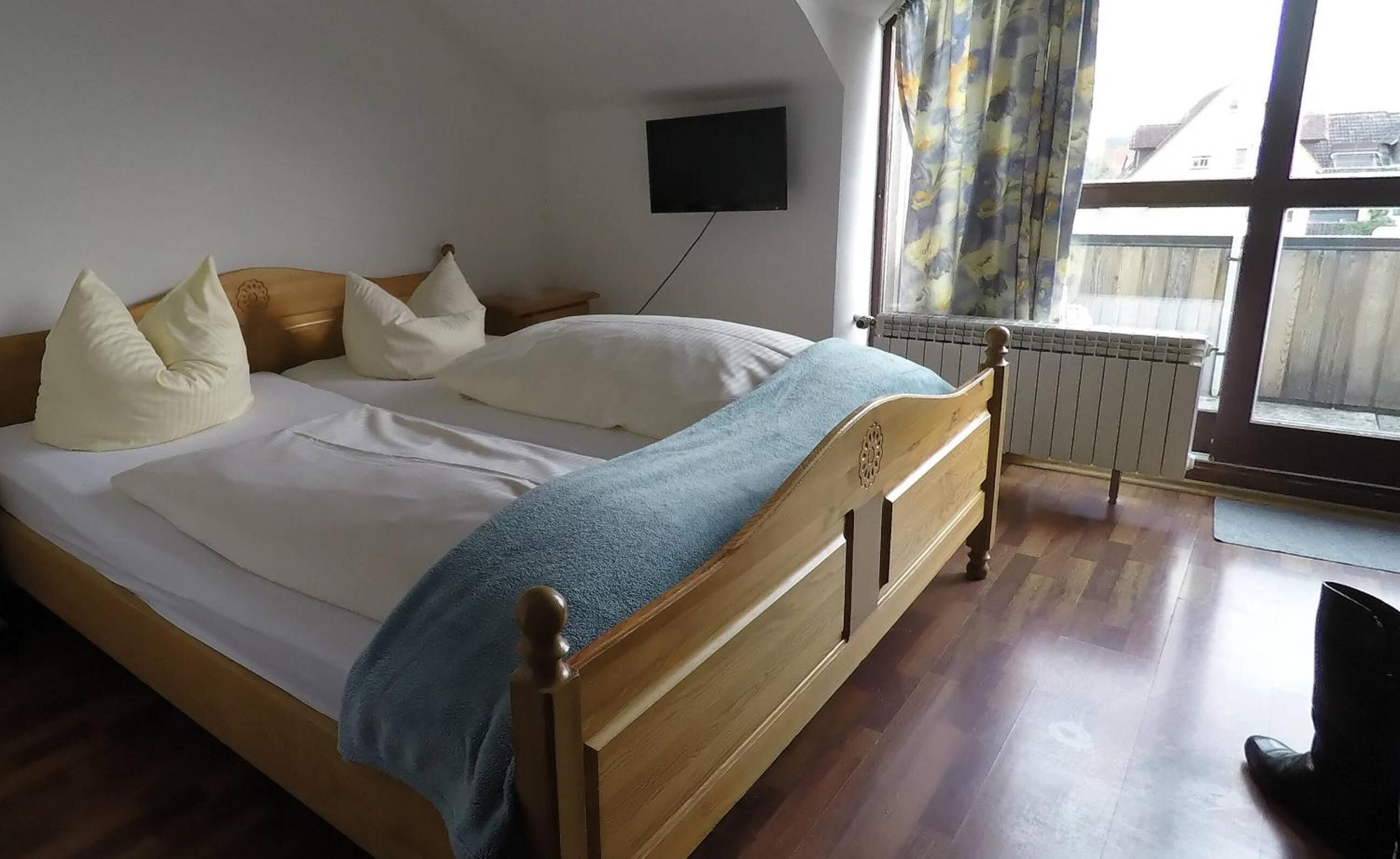 Un dormitorio con cama de madera, ropa de cama blanca, una manta azul y un televisor montado en la pared.