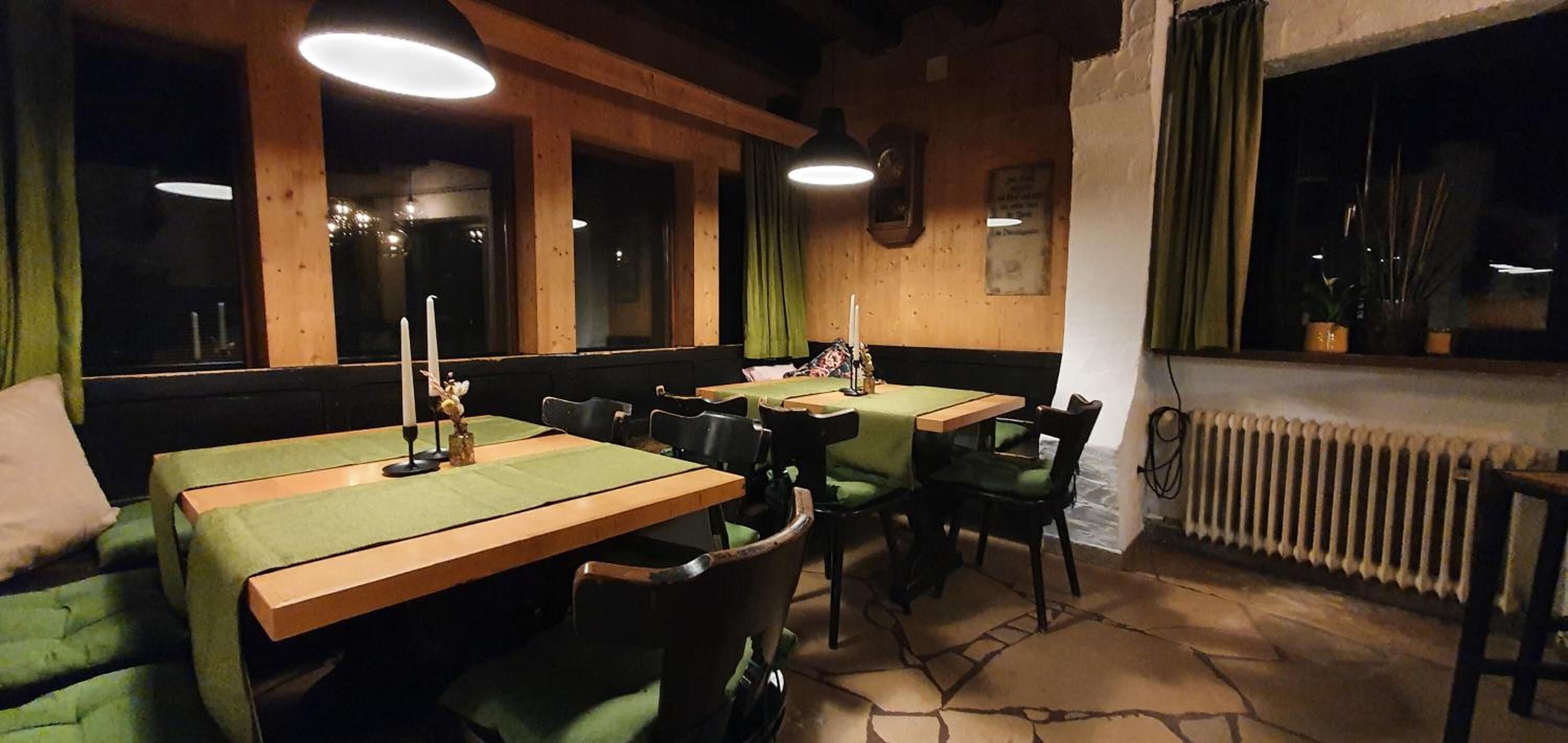 Een gezellig restaurant met houten tafels en groene fauteuils, met een stenen vloer en een raam met gordijnen.