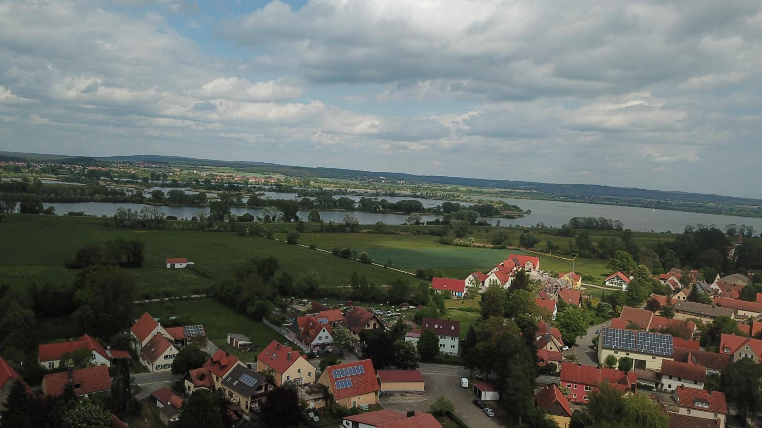 A village with red-roofed houses, a lake, and green fields.