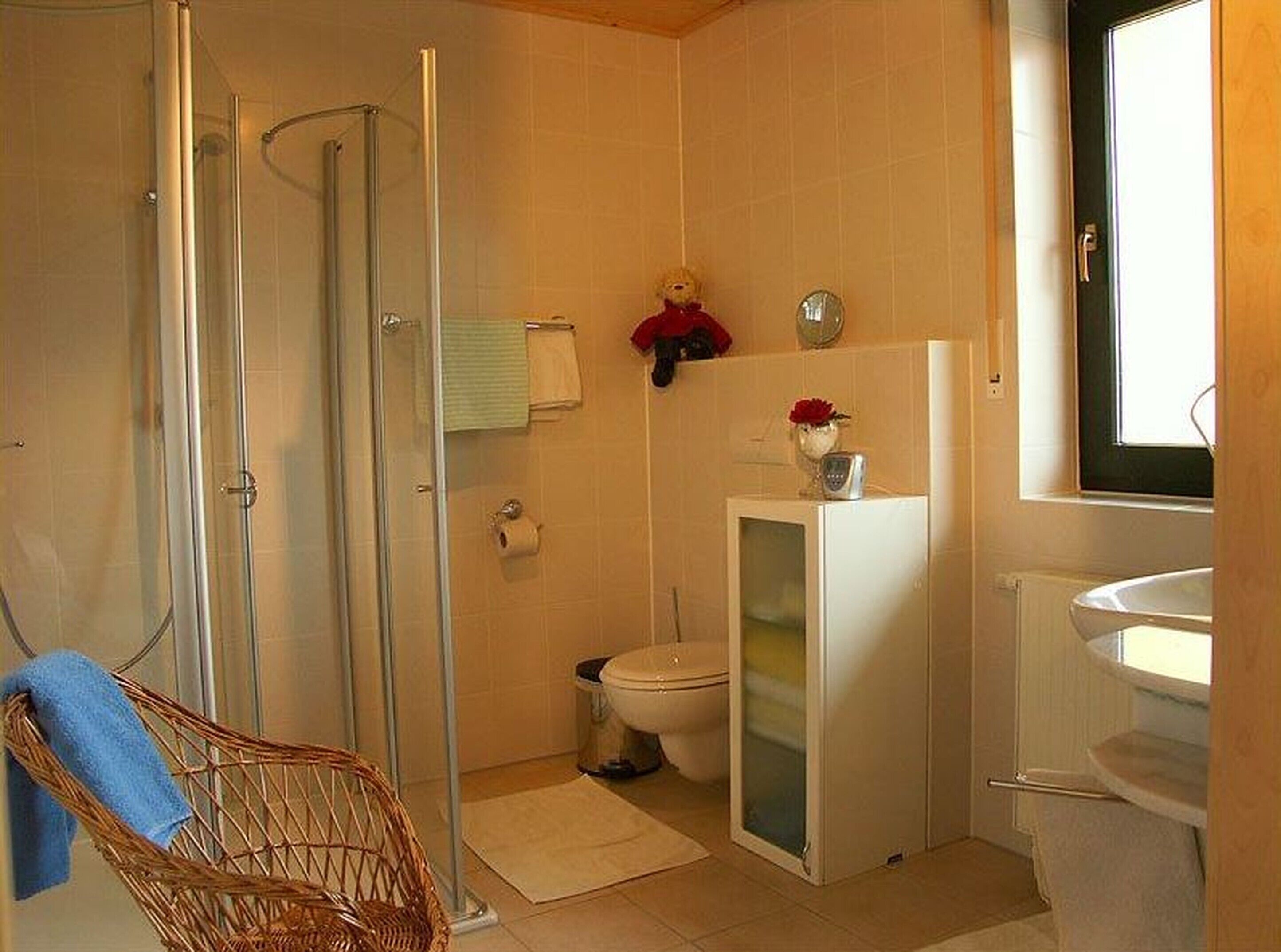 Um banheiro com box de vidro, vaso sanitário, pia e um pequeno armário.
