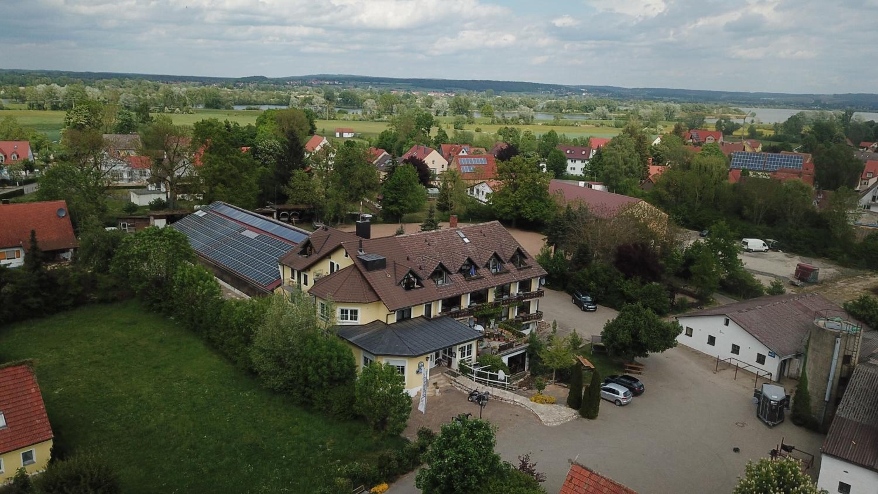 A residential area with houses, a large building with solar panels, and a view of a lake and hills.