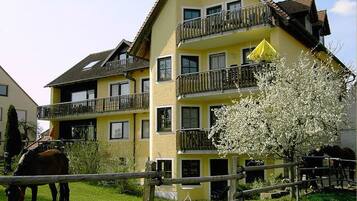 Un immeuble à plusieurs étages doté de balcons, un cheval dans un enclos et un arbre aux fleurs blanches.