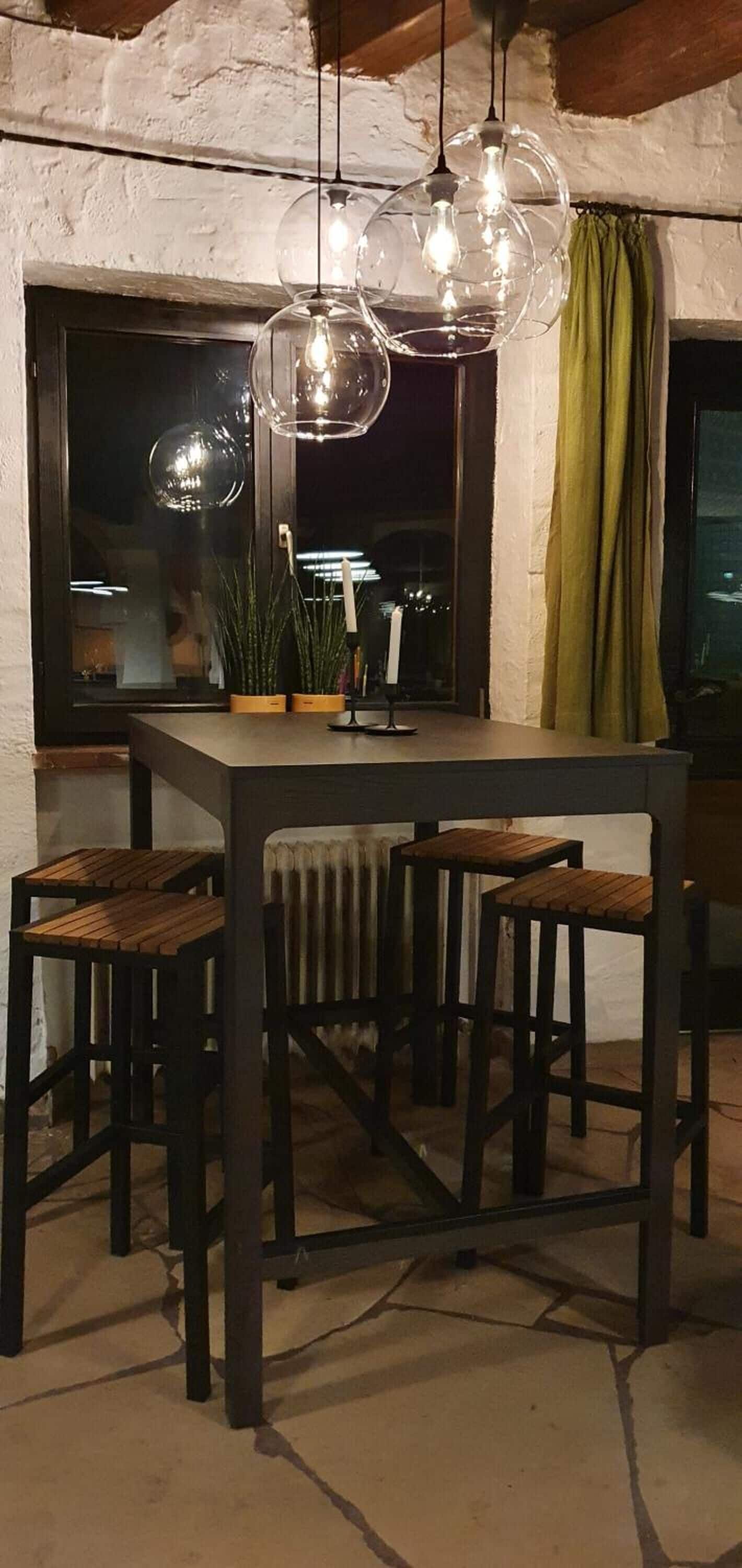 Un coin repas comprenant une table et quatre chaises, un luminaire suspendu et une fenêtre avec des rideaux.