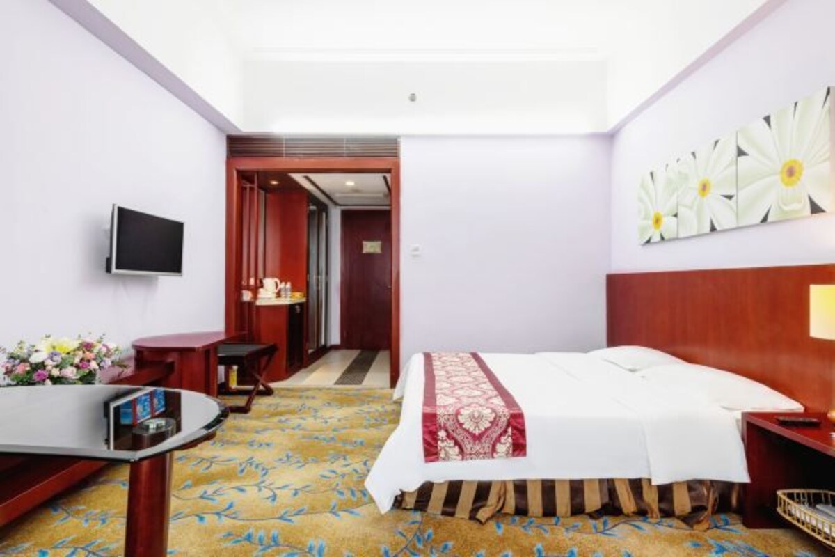 Una habitación de hotel con cama, escritorio, televisor y un cuadro en la pared.