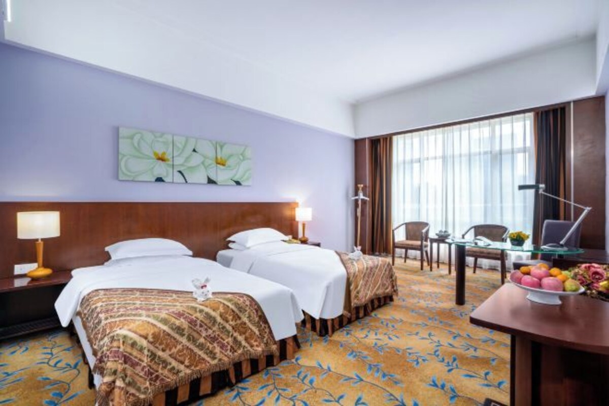Una habitación de hotel con dos camas, un escritorio con lámpara, una silla y un ventanal grande.