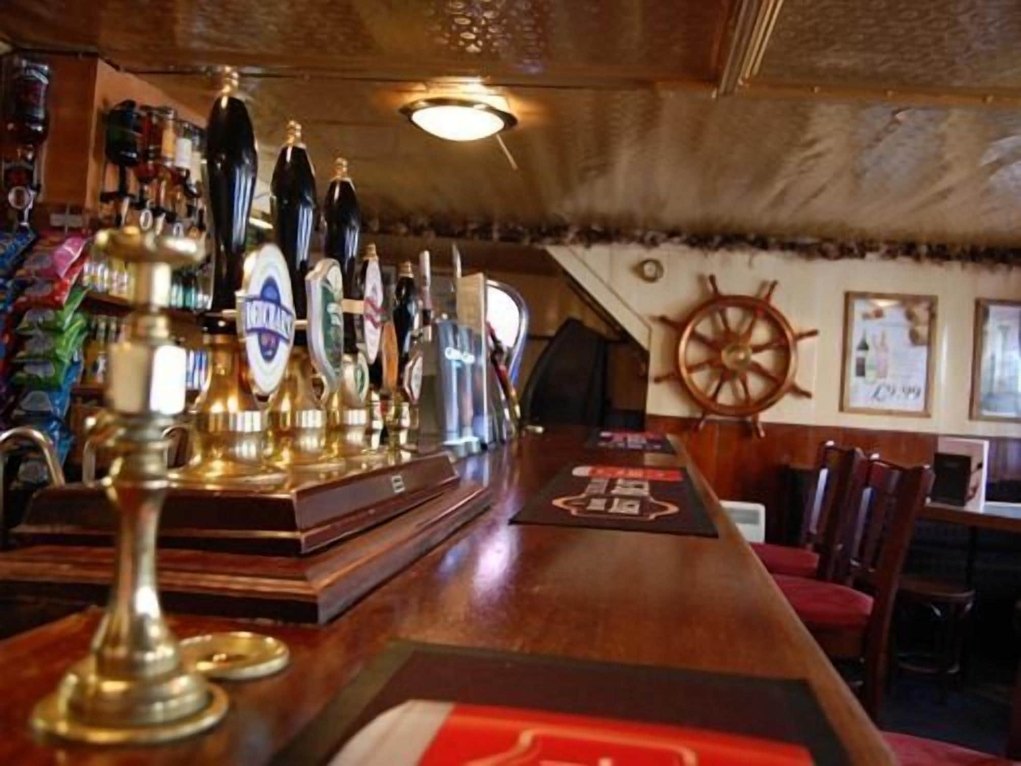 A bar area with a wooden counter, multiple beer taps, and a ship's wheel decoration on the wall.