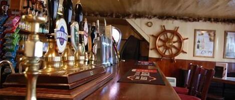A bar area with a wooden counter, multiple beer taps, and a ship's wheel decoration on the wall.