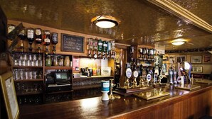 A bar with a wooden counter, multiple beer taps, and shelves with glassware. - Fisherman's Tavern Hotel - Inn by Greene King Inns (Dundee)