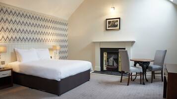 Habitación de hotel con una cama grande, una chimenea, una mesa de comedor con sillas y un papel tapiz estampado.