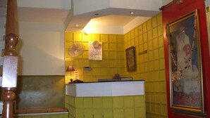 Una habitación con una decoración en tonos amarillo y blanco, un banco de madera, un ventilador, un calendario y un cuadro en la pared.