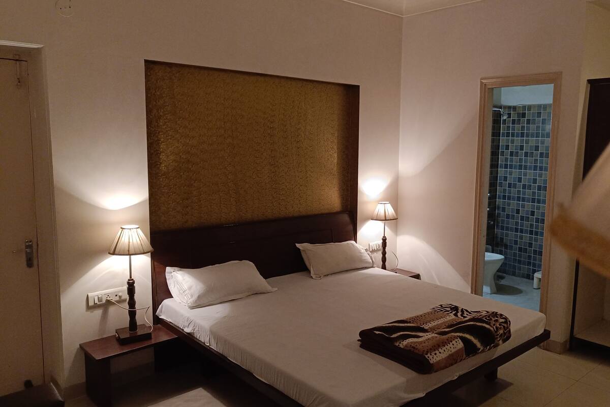 A bedroom with a large bed, two bedside lamps, a nightstand, and a view of the outside through a door.