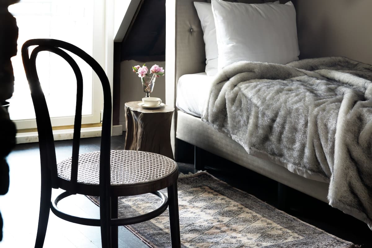 A bedroom with a sloped ceiling, a bed with a white blanket, a small table with a vase of flowers, and a chair.