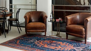 A living room with two brown leather armchairs, a patterned rug, a dining table with chairs, and a staircase in the background. - Boutique Hotel Grote Gracht (Maastricht)