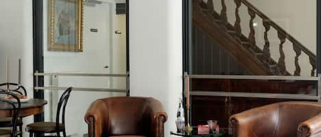 Una sala de estar con dos sillones de cuero marrón, un tapete estampado, una mesa de comedor con sillas y una escalera al fondo.
